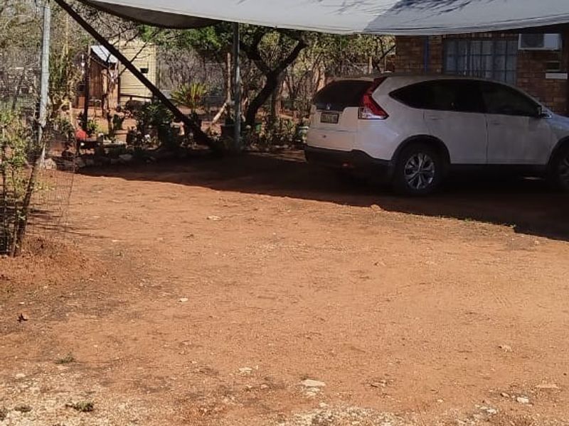 An exterior view of the property featuring a shaded parking area with a shade sail structure over an unpaved driveway.