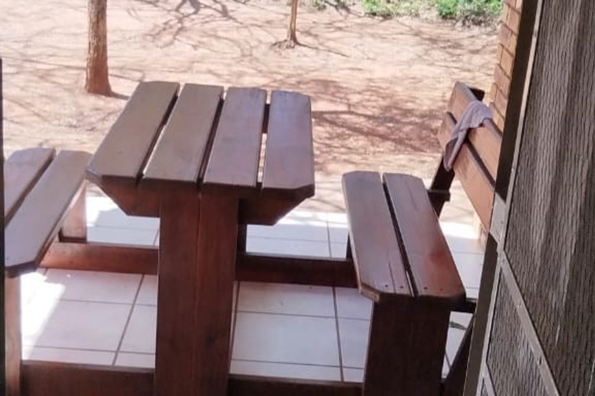A covered outdoor patio area featuring tiled flooring and exposed brickwork, overlooking a natural bushveld garden setting.