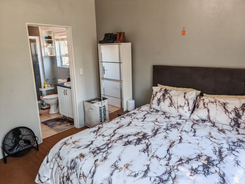 A bedroom featuring an en-suite bathroom with a vanity and shower, finished with tiled flooring.