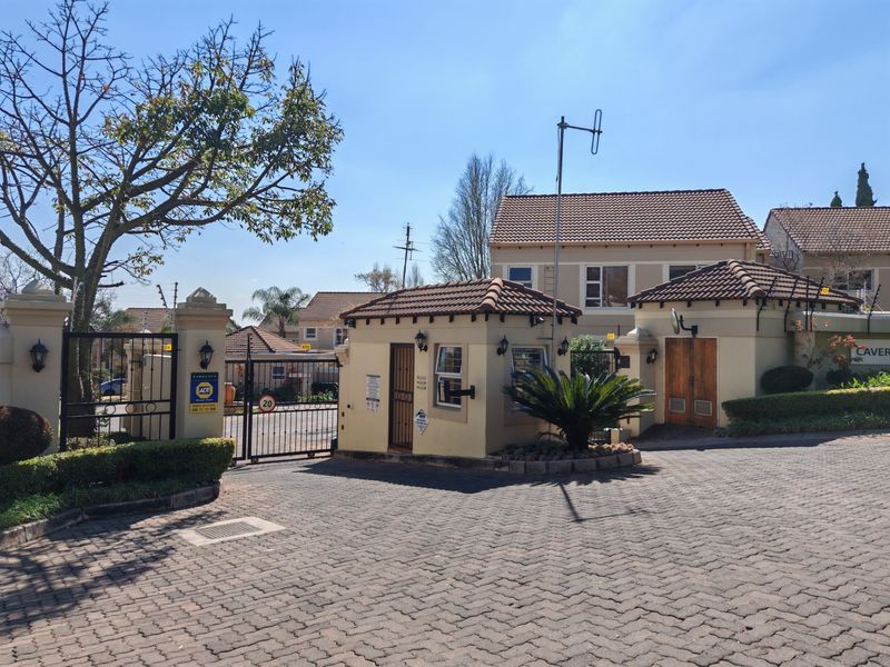 Front entrance view of the townhouse complex featuring a secure gated access point, guard house, and paved driveway.
