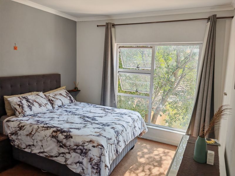 A well-lit bedroom featuring a large window with natural views, neutral wall tones, and classic coving detail.