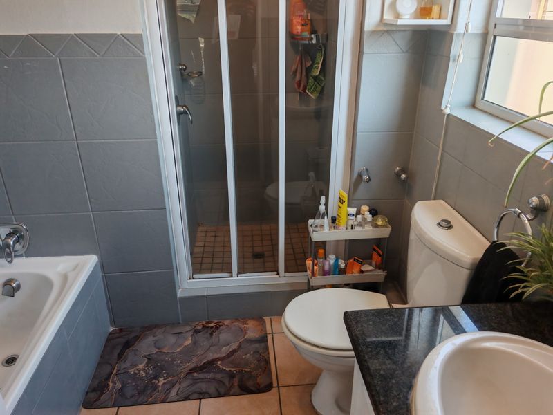 A functional bathroom featuring a shower enclosure, bathtub, toilet, and a vanity with a granite countertop, finished with grey wall tiles.