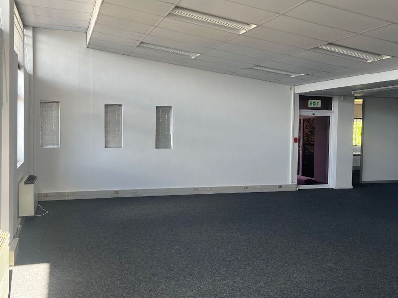 A spacious, empty office area featuring a suspended ceiling with recessed lighting, carpeted flooring, and wall-mounted air conditioning.