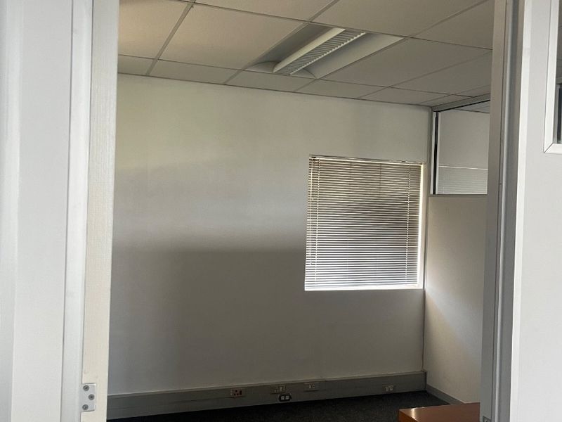 A vacant office space featuring a suspended ceiling, recessed lighting, carpeted flooring, and integrated electrical trunking along the base of the wall.