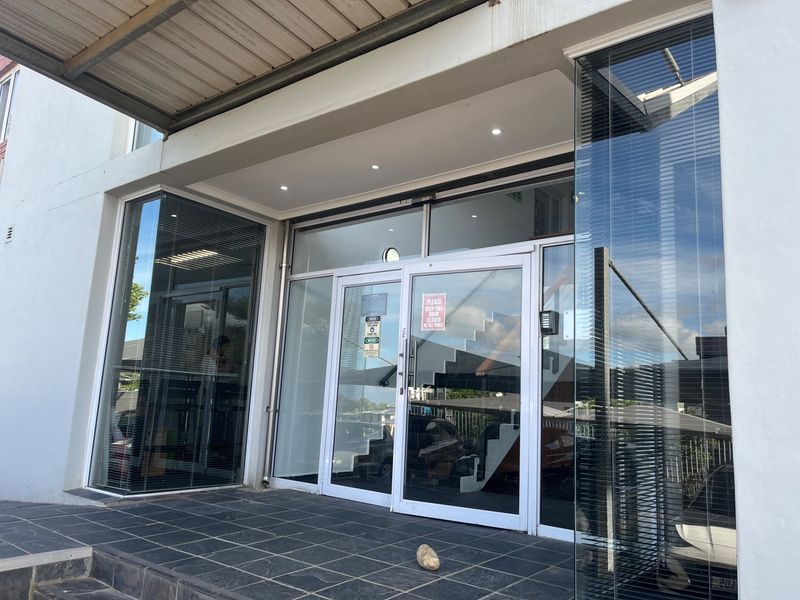 Modern office building entrance featuring a glass facade, tiled porch area, and recessed downlighting under a covered entryway.