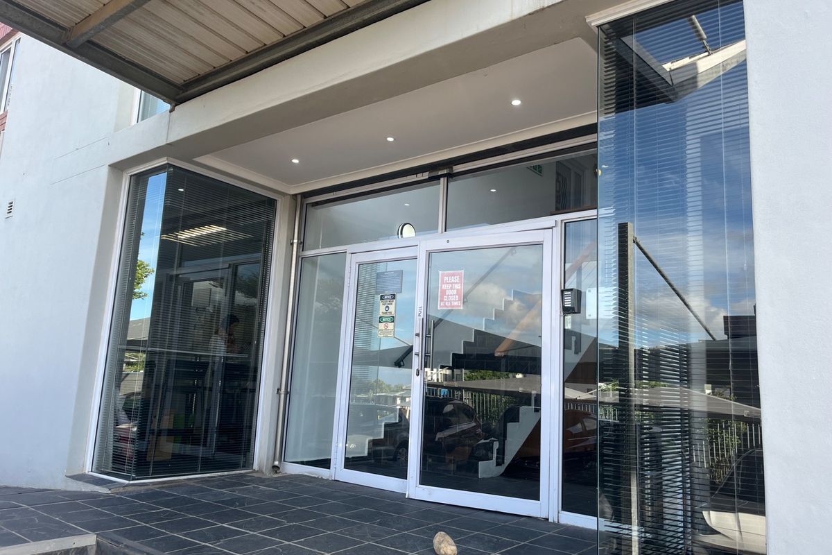 Modern office building entrance featuring a glass facade, tiled porch area, and recessed downlighting under a covered entryway.