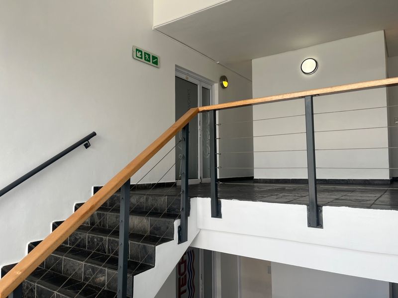 A clean and modern office hallway featuring a tiled staircase with a timber handrail and steel balustrade, leading to an upper landing area.