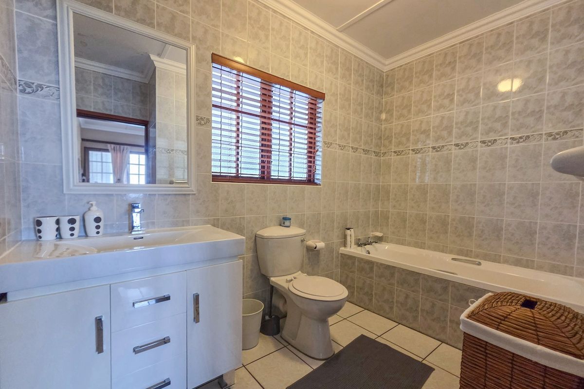 A functional bathroom featuring a vanity cabinet with basin, a standard toilet, and a tiled bathtub area with neutral wall and floor tiling.
