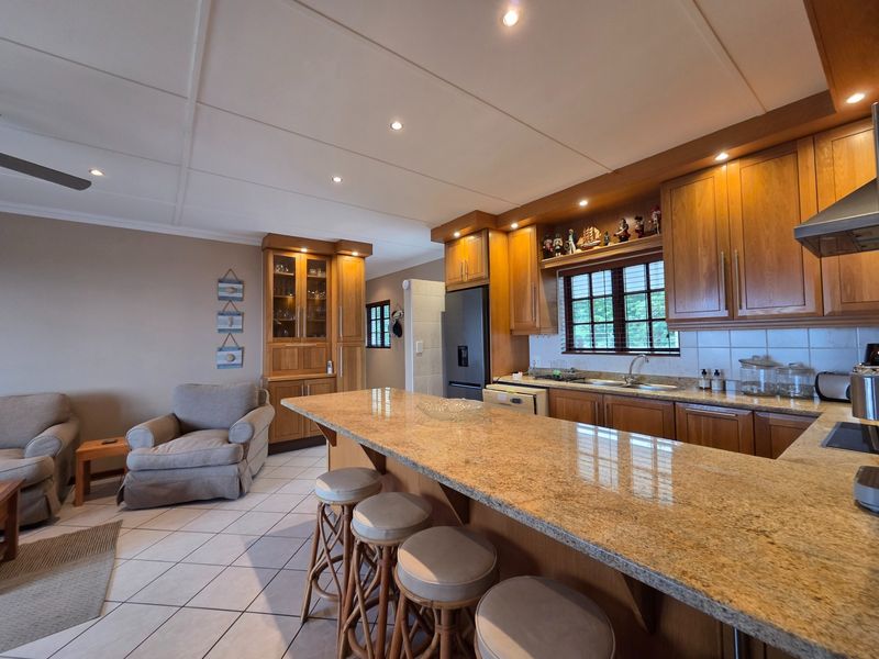Spacious open-plan kitchen and living area featuring warm wooden cabinetry, granite countertops, and tiled flooring, creating a functional and inviting home environment.