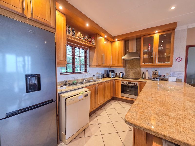 A well-maintained kitchen featuring warm wooden cabinetry, granite countertops, integrated stainless steel appliances, and tiled flooring with ample workspace.