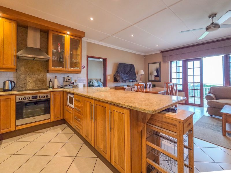 Open-plan living area featuring a well-appointed kitchen with granite countertops, wooden cabinetry, and integrated appliances, flowing into a dining and lounge space with balcony access.