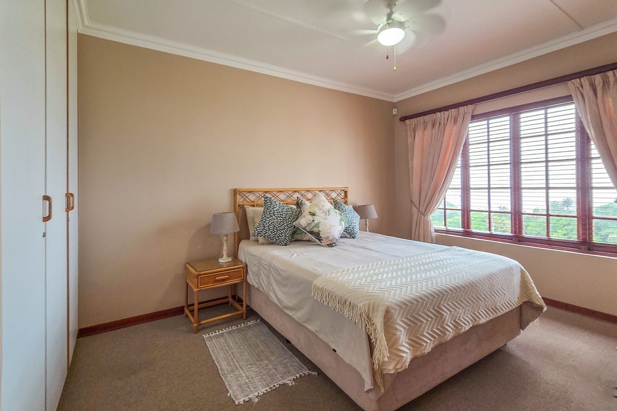 A well-maintained bedroom featuring built-in cupboards, a ceiling fan, and large windows with natural light, offering a comfortable and functional living space.