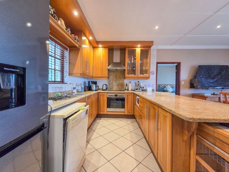 A well-maintained kitchen featuring warm wooden cabinetry, granite countertops, built-in oven, extractor fan, and tiled flooring with an open-plan layout.