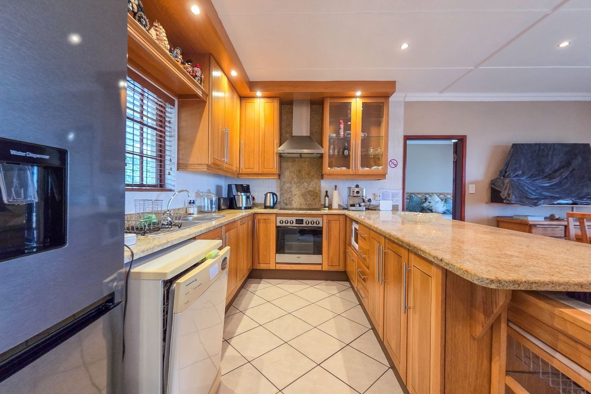 A well-maintained kitchen featuring warm wooden cabinetry, granite countertops, built-in oven, extractor fan, and tiled flooring with an open-plan layout.