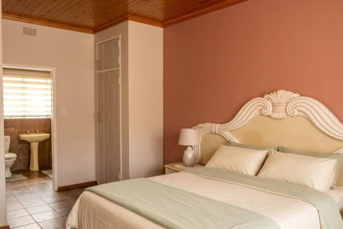A bedroom featuring a timber ceiling, tiled flooring, and a built-in cupboard, with an adjoining en-suite bathroom.