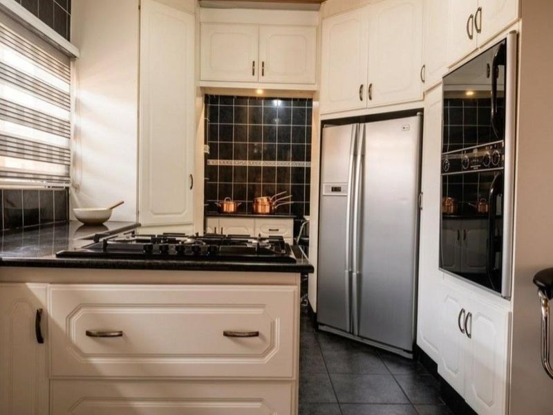 A well-maintained kitchen featuring white cabinetry, dark tiled backsplash, stone countertops, and integrated stainless steel appliances.