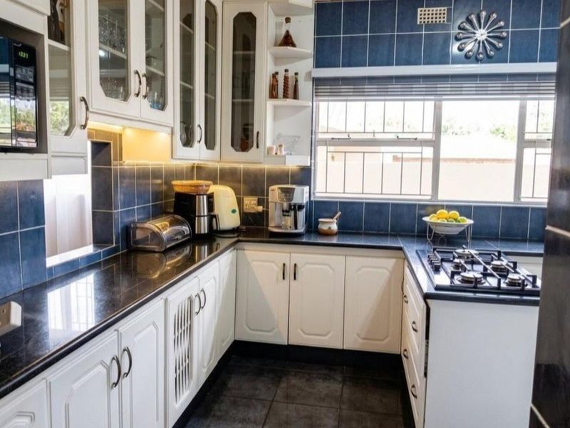 A functional kitchen featuring white cabinetry, dark granite countertops, a gas hob, and blue tiled backsplash with under-cabinet lighting.