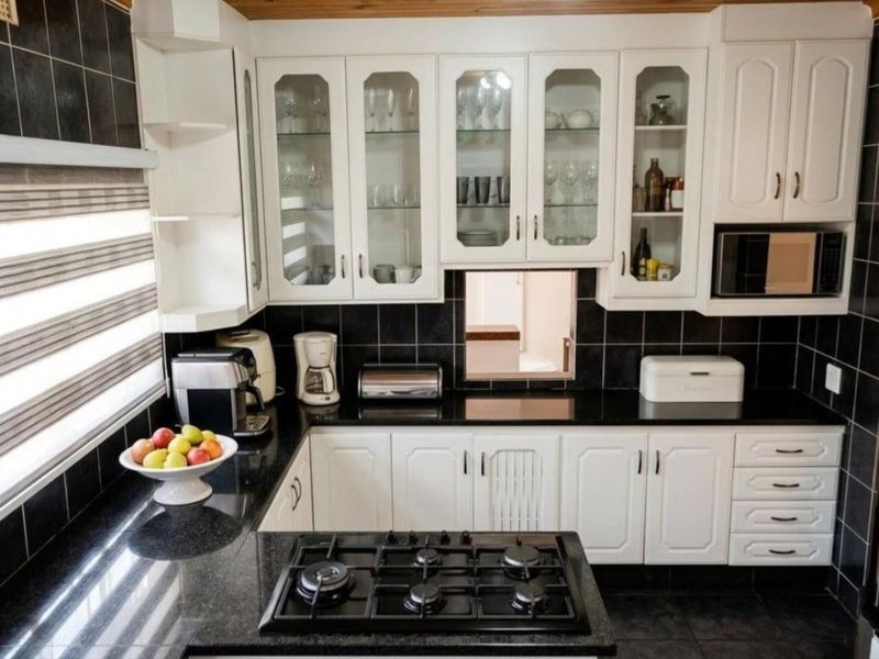 A well-maintained kitchen featuring white cabinetry, black granite countertops, a gas hob, and a striking black tiled backsplash with timber ceiling accents.