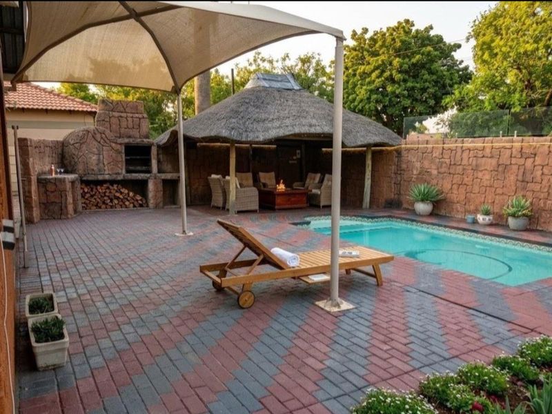 Outdoor entertainment area featuring a swimming pool, a thatched lapa, and a built-in braai, set within a paved courtyard with stone-clad boundary walls.