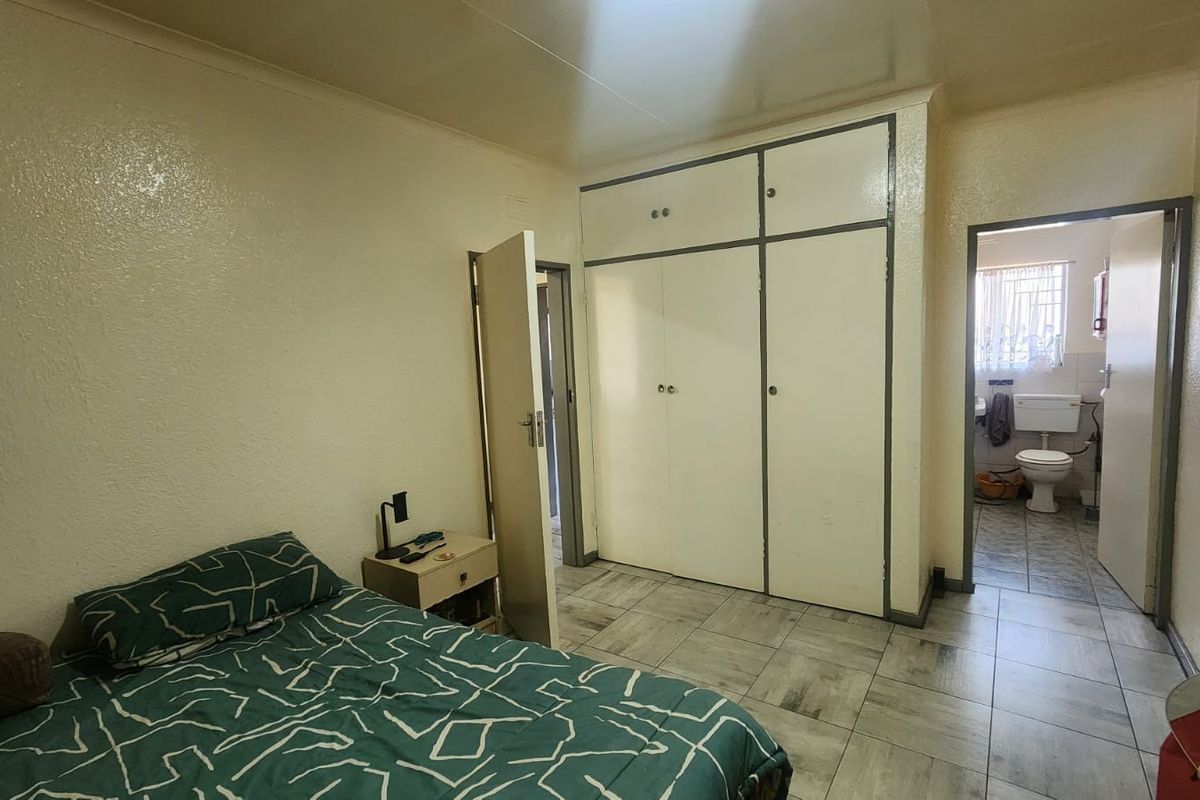 A bedroom featuring built-in cupboards and tiled flooring, with an adjoining bathroom visible through the doorway.