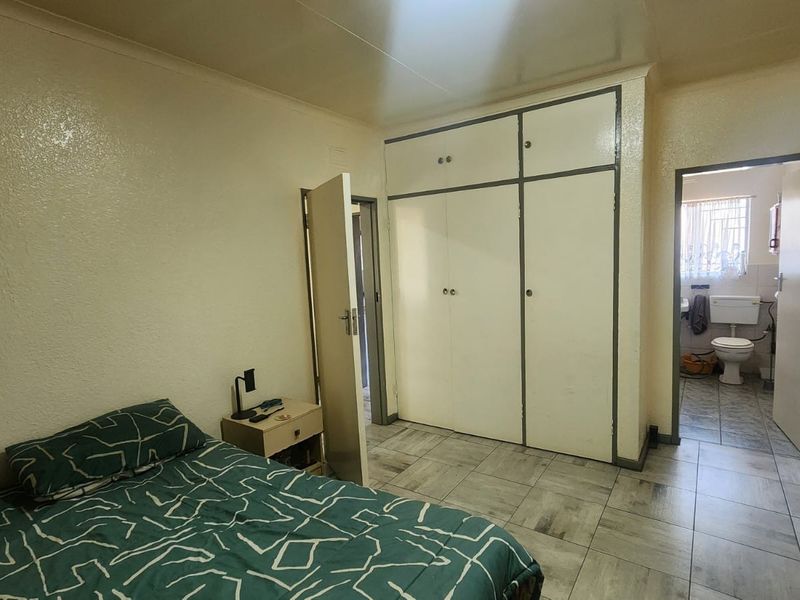 A bedroom featuring built-in cupboards and tiled flooring, with an adjoining bathroom visible through the doorway.