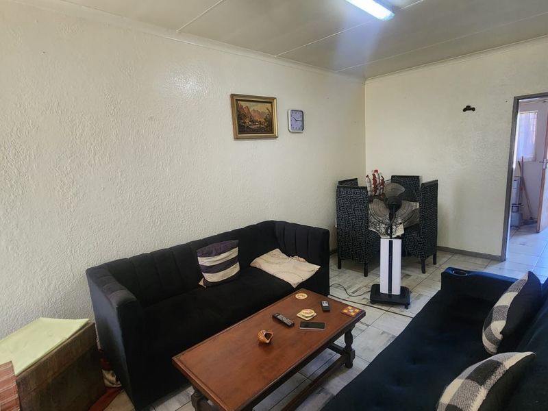 A living room area featuring tiled flooring and basic lighting, presenting a dated aesthetic that could benefit from modern updates and refreshed wall finishes.