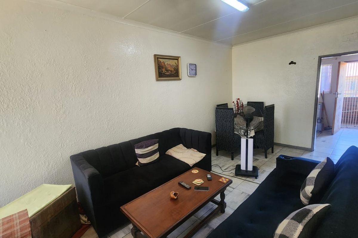 A living room area featuring tiled flooring and basic lighting, presenting a dated aesthetic that could benefit from modern updates and refreshed wall finishes.