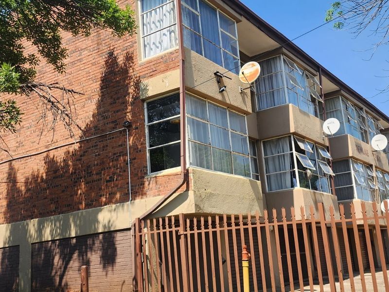 Exterior view of a multi-story apartment building featuring brick facade, metal window frames, and perimeter security fencing.