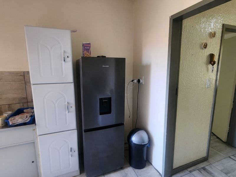 A compact kitchen area featuring a sink, tiled backsplash, and built-in cabinetry, showing signs of wear and requiring cosmetic updates.
