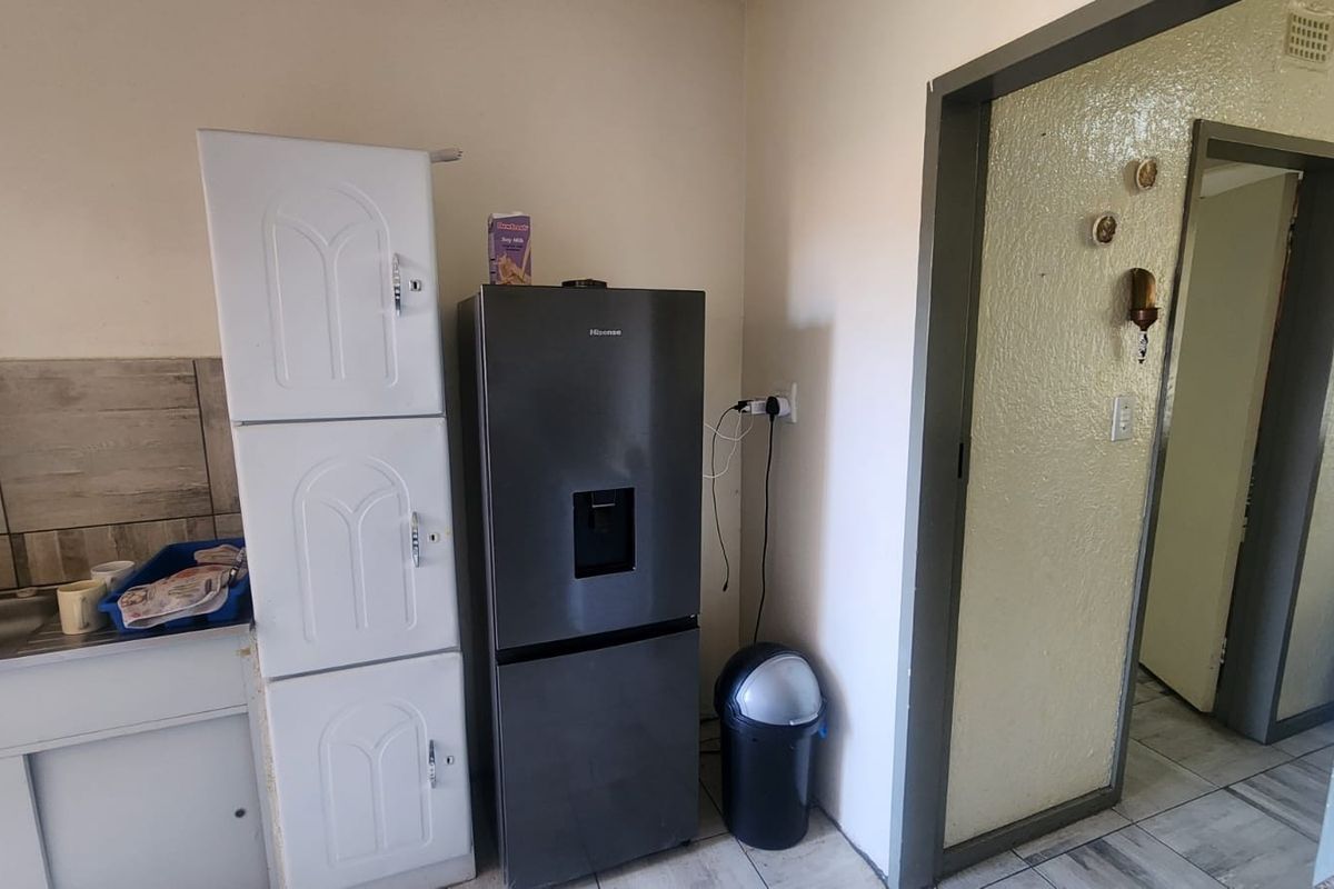 A compact kitchen area featuring a sink, tiled backsplash, and built-in cabinetry, showing signs of wear and requiring cosmetic updates.