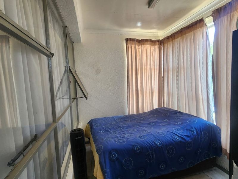 A bedroom featuring textured walls, tiled flooring, and large aluminium-framed windows with curtains.
