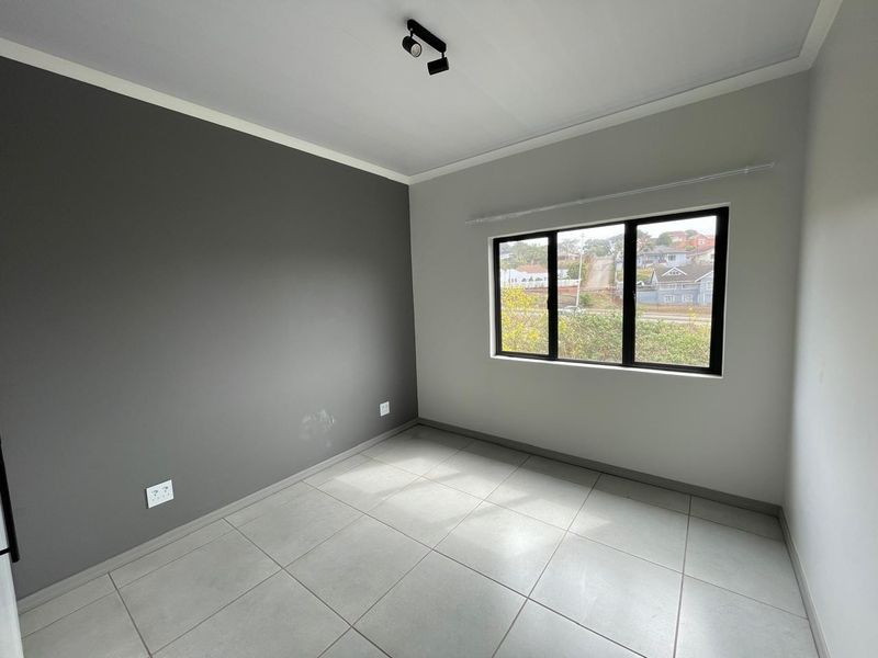 A bright, empty bedroom featuring neutral tiled flooring, a modern dark grey accent wall, and black-framed windows with natural light.