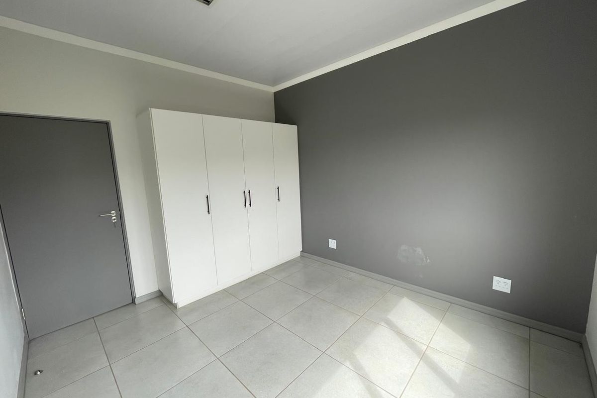A clean, empty bedroom featuring neutral tiled flooring, a built-in white wardrobe, and a grey accent wall.