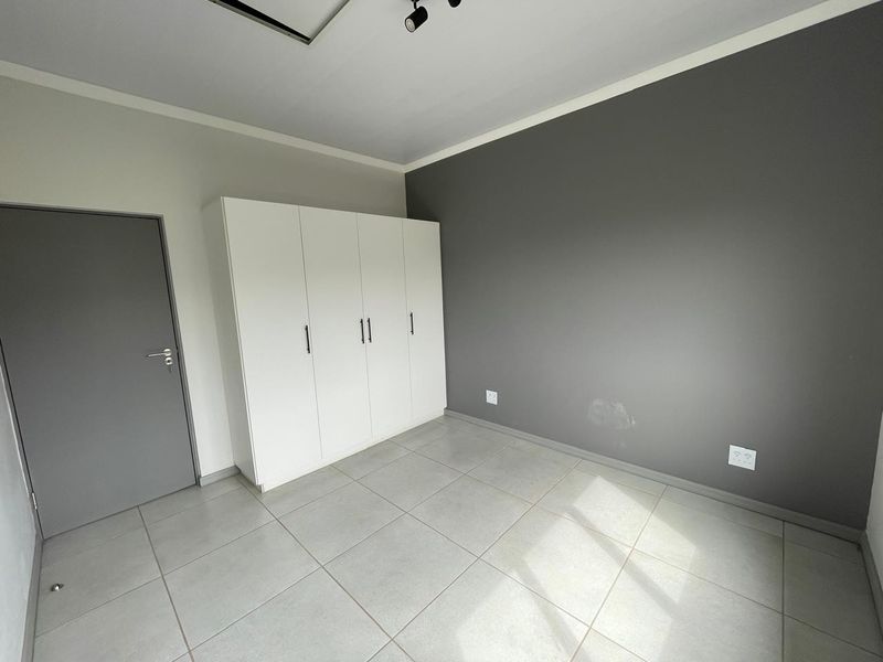 A clean, empty bedroom featuring neutral tiled flooring, a built-in white wardrobe, and a grey accent wall.