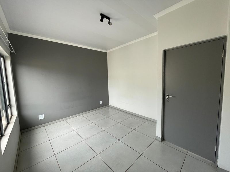 A clean, empty bedroom featuring neutral grey and white walls, large format floor tiles, and a modern grey interior door.
