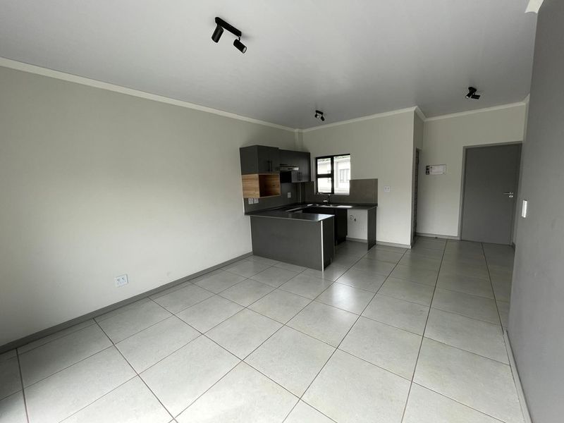 An open-plan living and kitchen area featuring modern grey cabinetry, tiled flooring, and contemporary track lighting in a clean, vacant space.