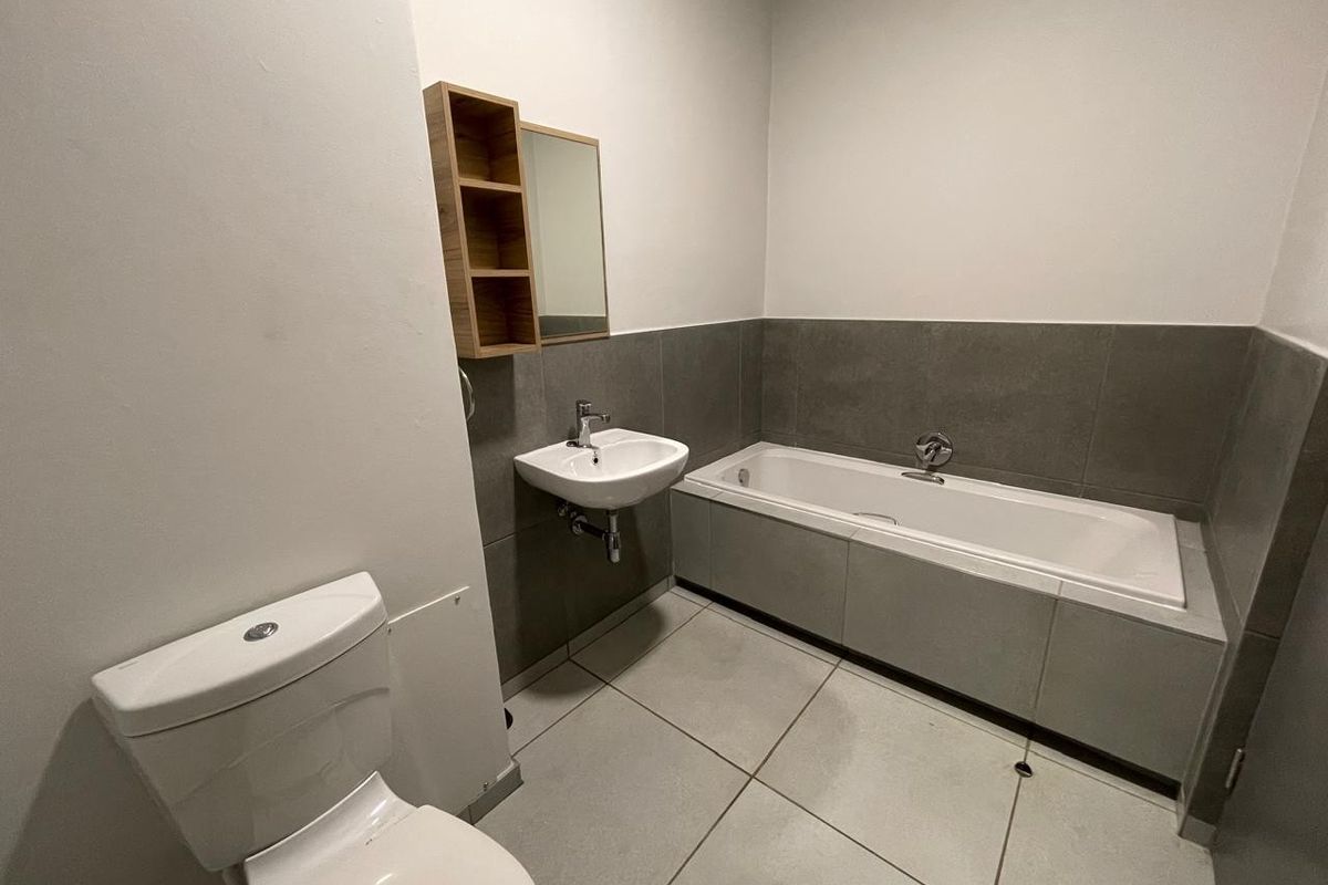A clean, modern bathroom featuring a built-in bathtub, wall-mounted basin, and toilet with neutral grey floor and wall tiling.