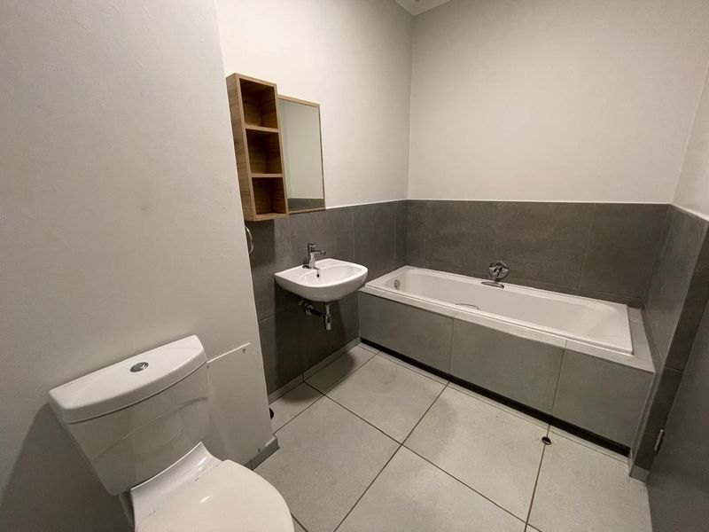A clean, modern bathroom featuring a built-in bathtub, wall-mounted basin, and toilet with neutral grey floor and wall tiling.