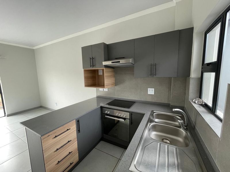 Modern kitchen featuring sleek grey and wood-tone cabinetry, stone countertops, integrated stainless steel sink, and built-in electric oven with hob.