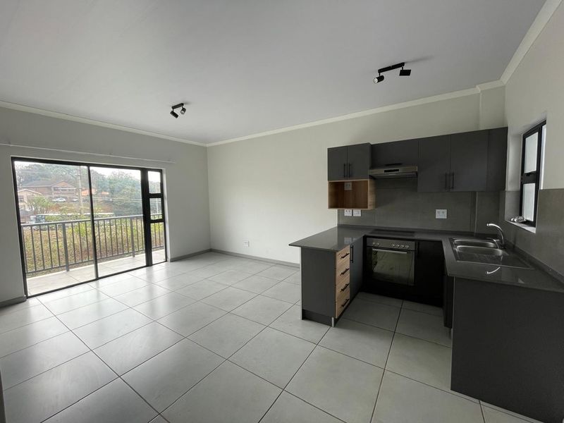 Modern open-plan living area featuring a sleek kitchen with dark cabinetry, stone countertops, integrated appliances, and large sliding doors leading to a balcony.