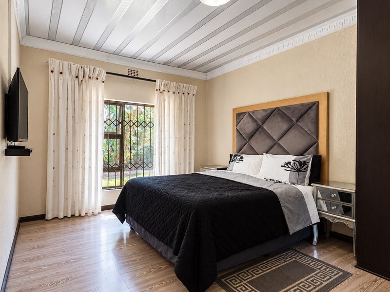 A well-maintained bedroom featuring laminate flooring, decorative ceiling panels, crown molding, and a built-in wardrobe with security bars on the window.