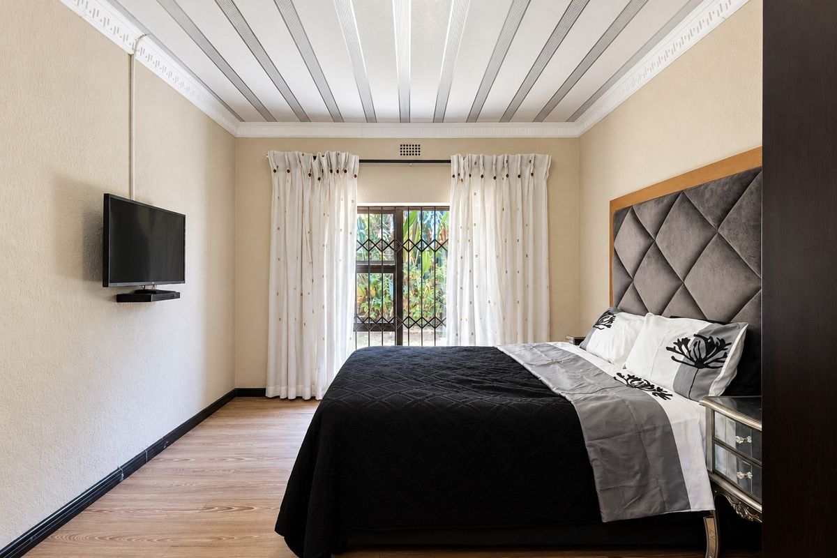 A well-maintained bedroom featuring laminate flooring, decorative ceiling molding, and a secure window with a metal security gate.