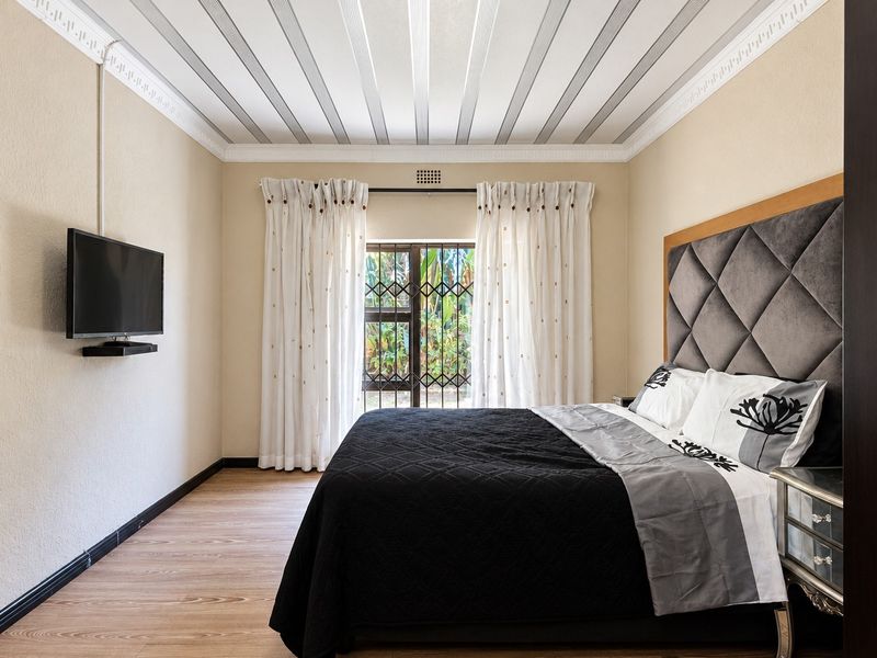 A well-maintained bedroom featuring laminate flooring, decorative ceiling molding, and a secure window with a metal security gate.