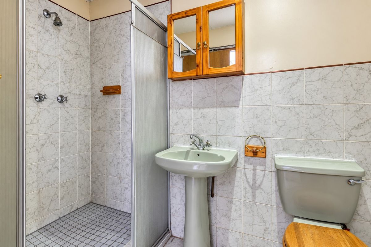 A functional bathroom featuring a shower enclosure, pedestal basin, and toilet with dated finishes, offering potential for a modern renovation.
