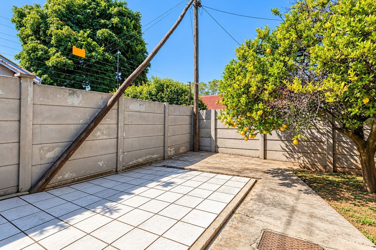 A rear outdoor area featuring a tiled patio, concrete paving, and a precast concrete boundary wall with electric fencing.