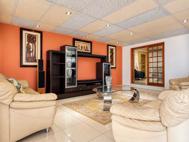 A spacious living room featuring tiled flooring, recessed downlights, and a suspended ceiling, with a wooden sliding door leading to an adjacent room.
