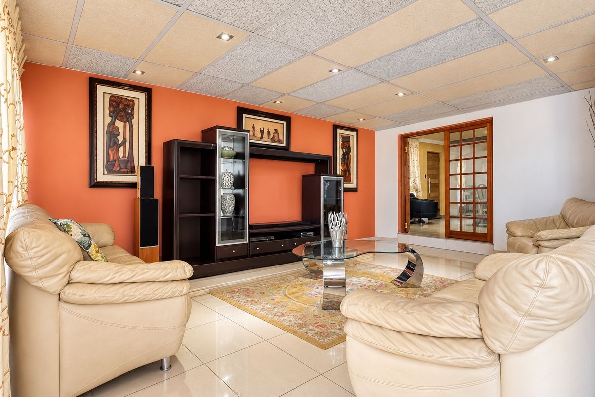 A spacious living room featuring tiled flooring, recessed downlights, and a suspended ceiling, with a wooden sliding door leading to an adjacent room.