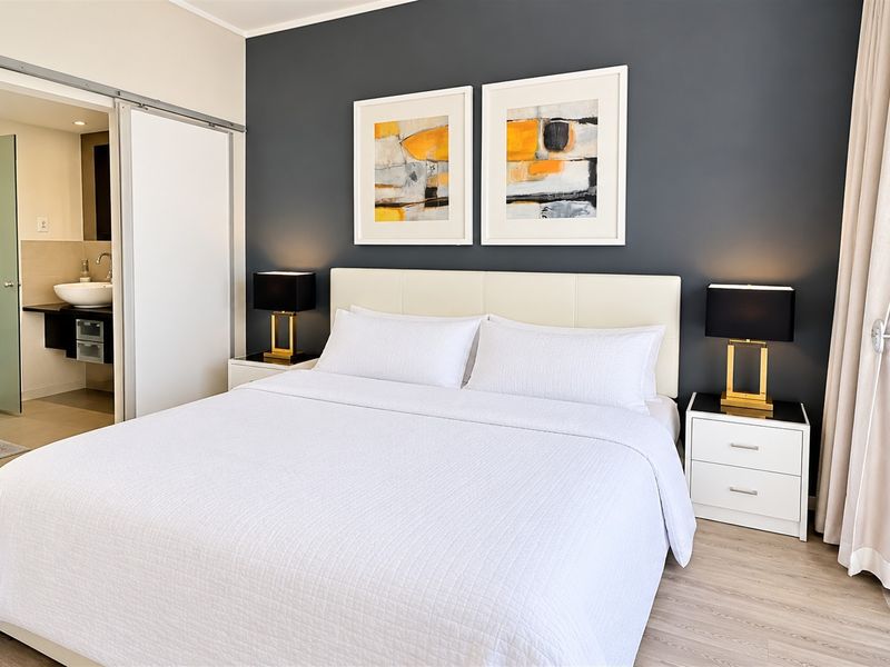 A well-maintained bedroom featuring modern laminate flooring, a dark accent wall, and an adjoining en-suite bathroom accessed via a sliding door.