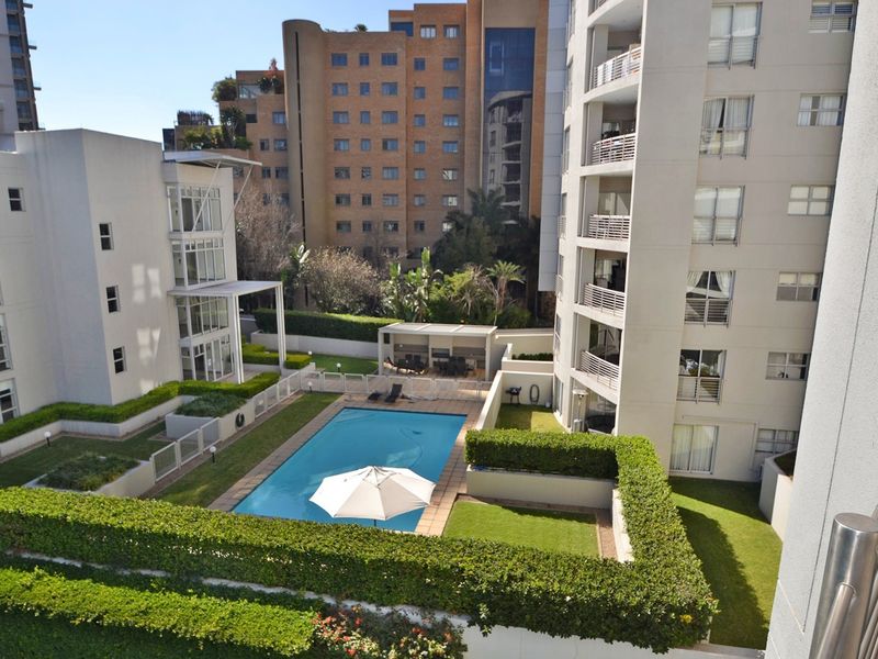 Elevated view of a well-maintained apartment complex courtyard featuring a swimming pool, landscaped gardens, and a communal outdoor entertainment area.