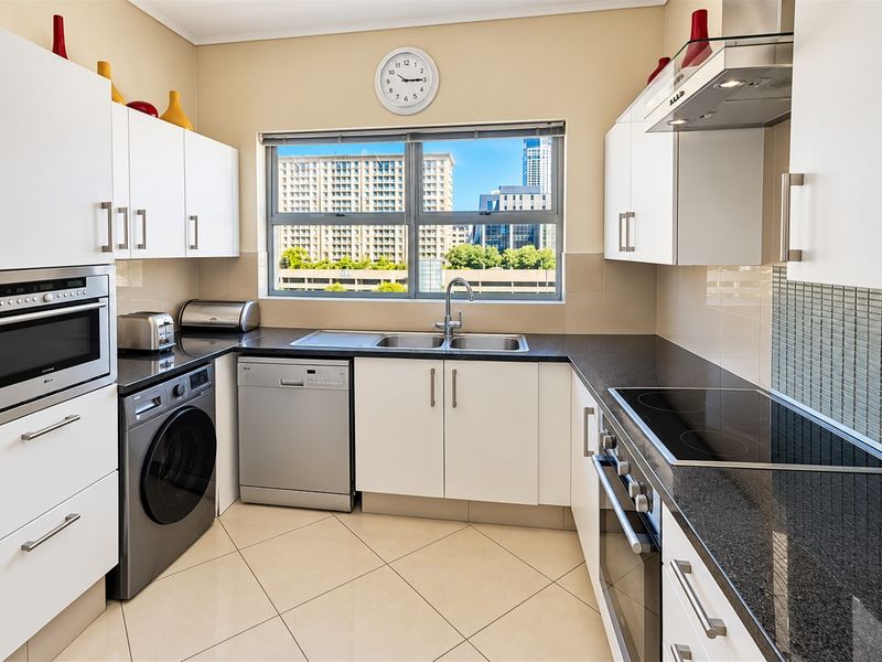 Modern kitchen featuring granite countertops, built-in oven, electric hob, extractor fan, and ample cabinetry, with a window providing natural light and urban views.